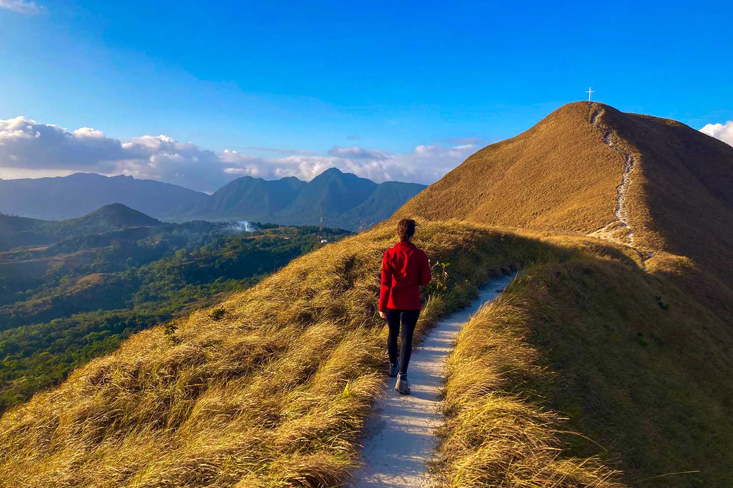 Ein Frau wandert auf einen Berg. Oben steht ein Gipfelkreuz. Man hat einen Panoramablick auf das Valle de Anton in Panama